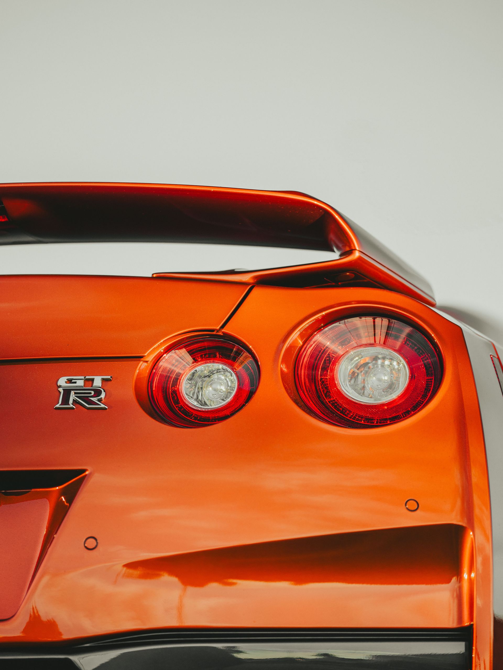 Detailed image of a Nissan GT-R R35's rear end with vibrant orange color and iconic taillights.