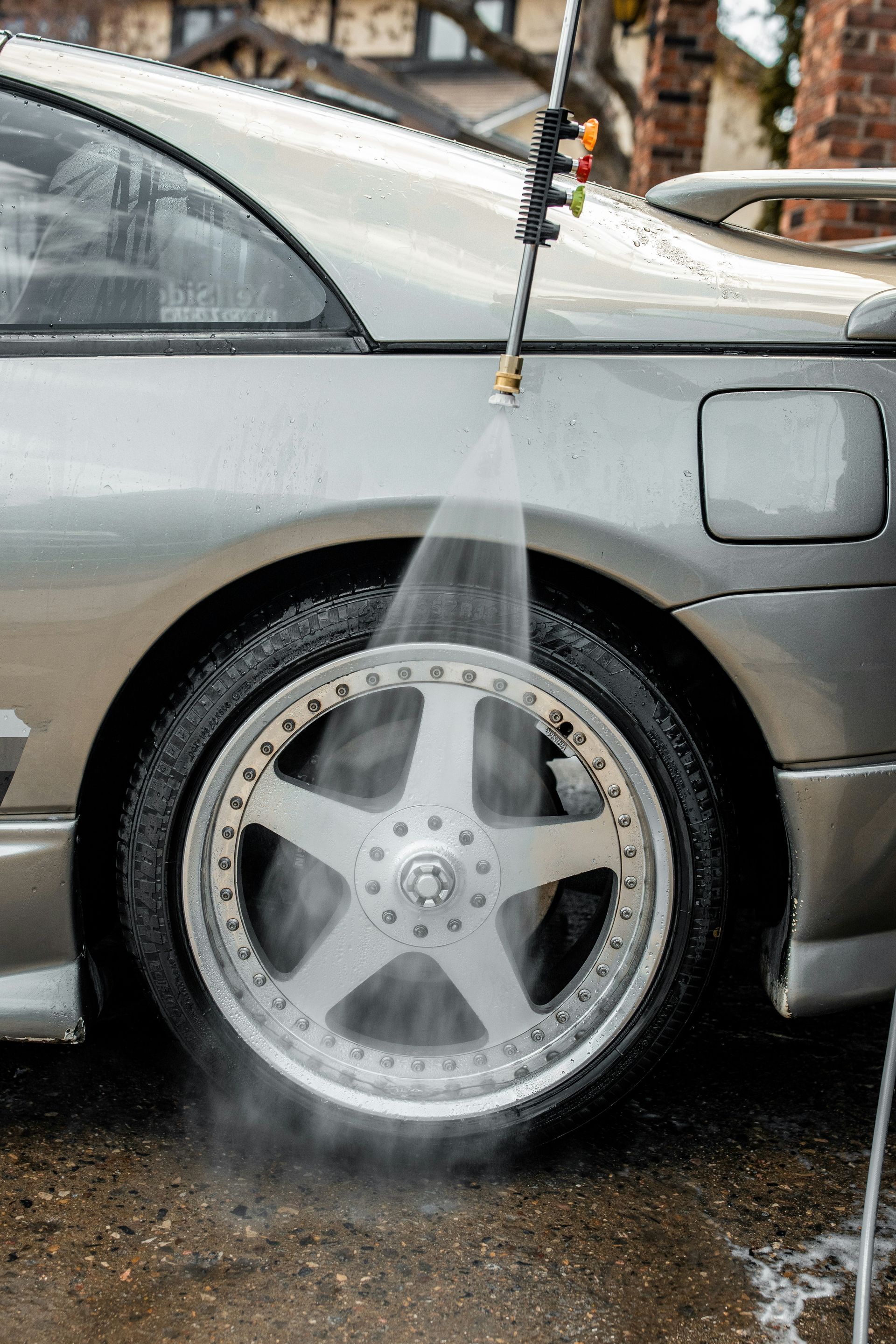 Person washing a silver car wheel with a pressure washer
