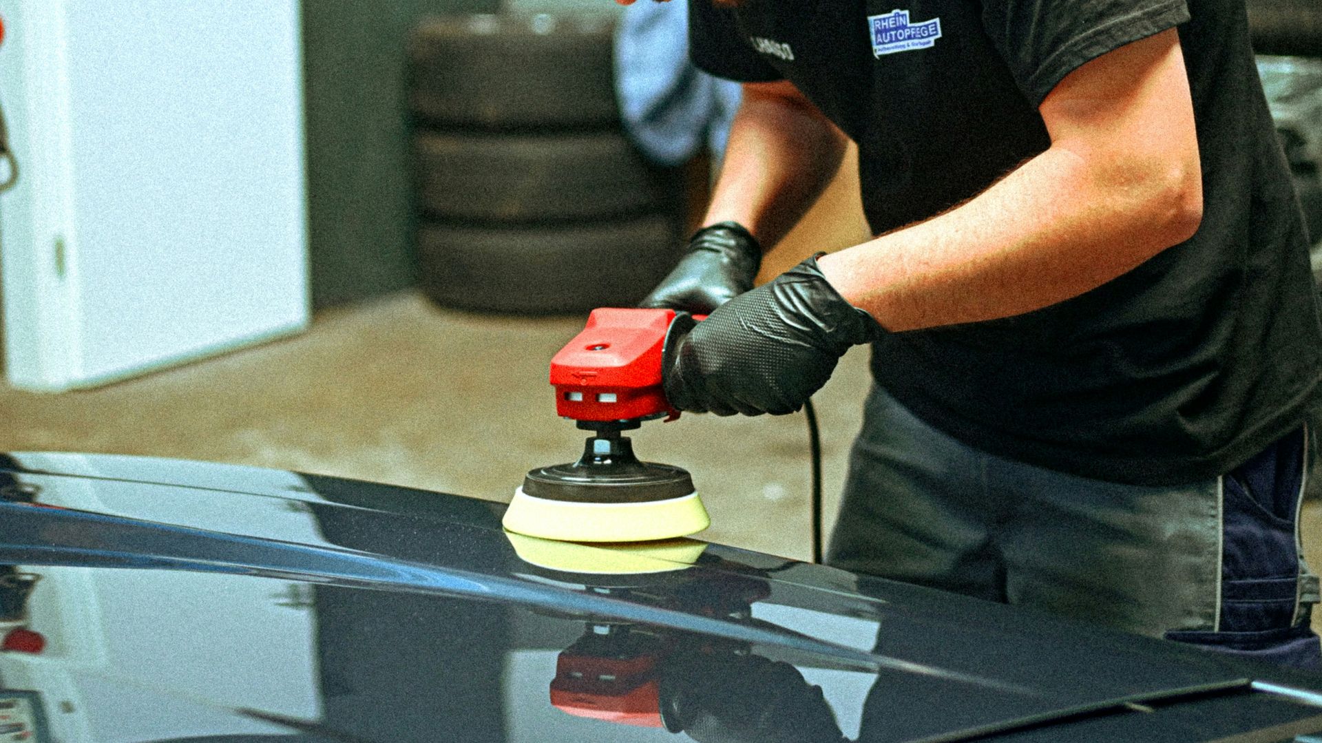 A person polishes a dark car with an electric polisher.