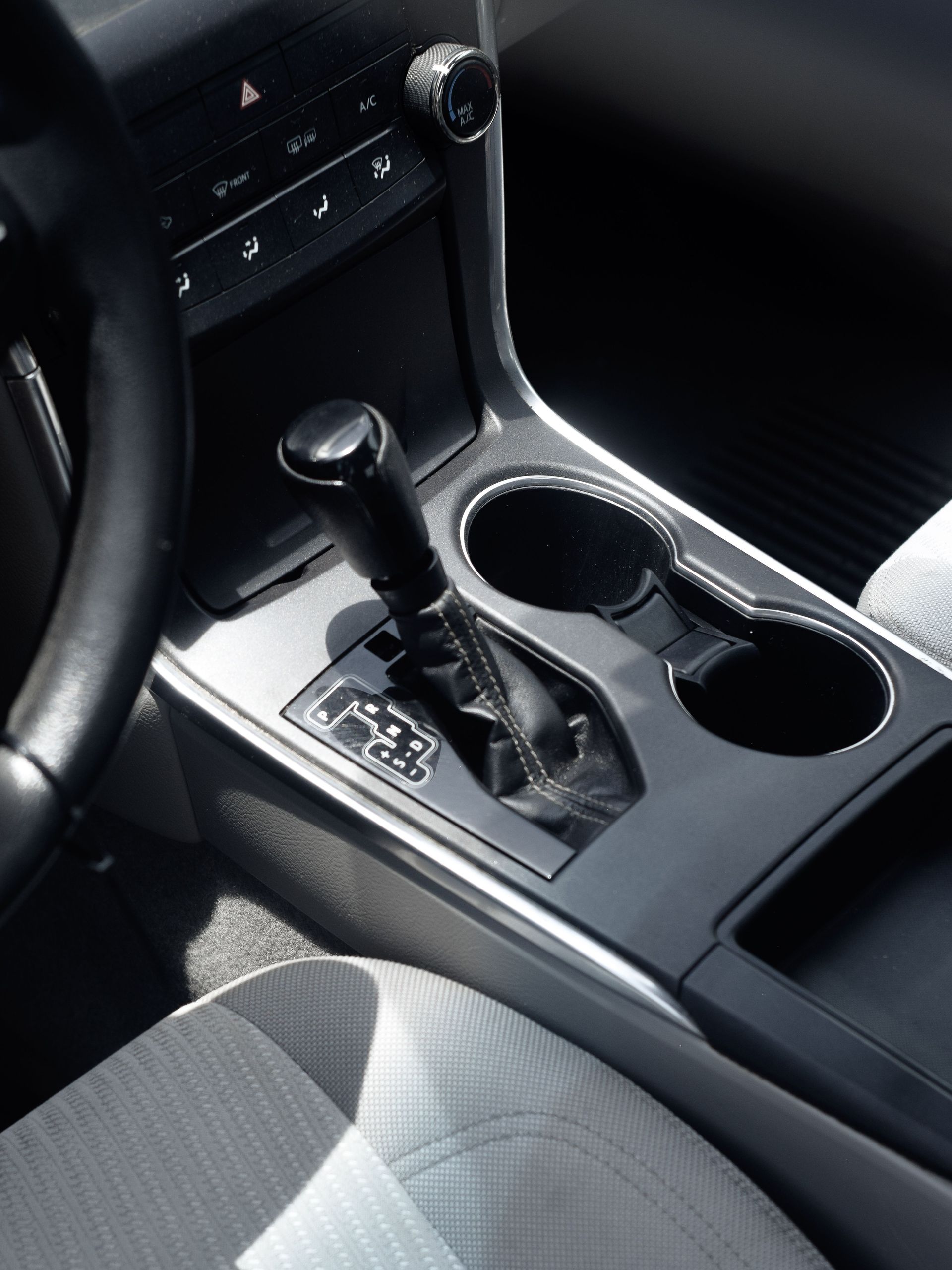 Close-up of a car's interior showing gear shift, cup holders, and steering wheel under daylight.